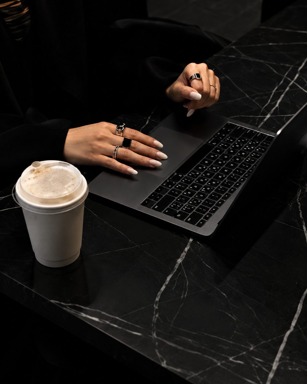 A person working on a laptop at a dark desk with a coffee cup, representing digital marketing work.